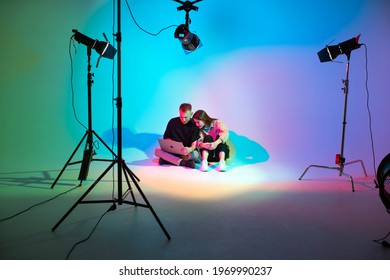 Creative team young girl and boy with laptop working in photostudio with photography equipment. Colorful neon light