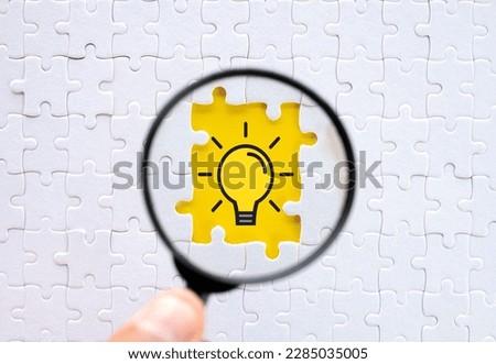 Creative Thinking idea and Innovation concept.,Hand holding magnifying glass focus on missing white jigsaw and puzzle with light bulb icon.