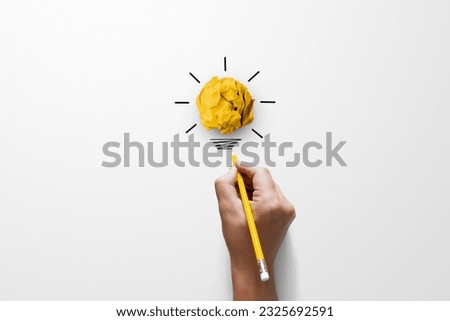 Creative thinking ideas and innovation concept. Paper scrap ball yellow colour with light bulb symbol on white background and hand holding yellow pencil