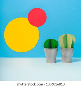 Creative three dimensional paper cactuses on vivid blue background with yellow and pink circles. Pots with fake succulent plants for office design. Exotic summer concept. Side view, copy space.