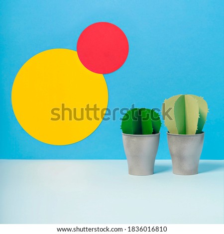 Creative three dimensional paper cactuses on vivid blue background with yellow and pink circles. Pots with fake succulent plants for office design. Exotic summer concept. Side view, copy space.