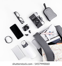 Creative top view flat lay of open backpack with laptop and tablet inside, mobile phone map copy space white background minimal style. Concept of modern man accessories for travel adventures and life