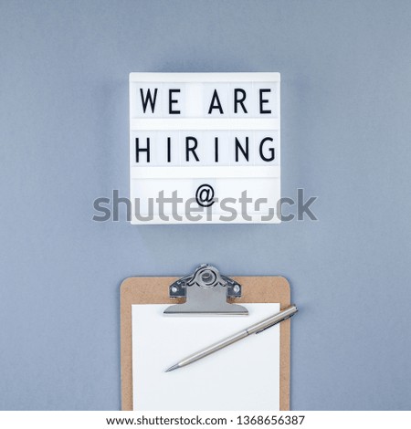 Creative top view flat lay of desk with we are hiring text on lightbox with copy space on blue background in minimal style. Concept of new job, hiring recruitment process, new team members screening
