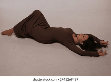 Creative upside down portrait of young beautiful brunette woman lying on her back on the floor in studio. Natural beauty, minimalist fashion and feminine lifestyle concept