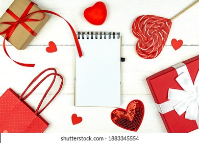 Creative Valentine Day romantic composition with red hearts, satin ribbon, lollipop, gift box and paper bag on white background. Mockup with copy space for blogs and social media