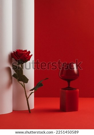 Creative Valentine's Day composition with red glass and red rose flower on red and white background. Minimal luxury spring or summer party concept.