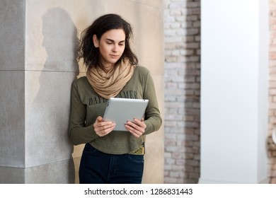 Creative woman using tablet computer standing leaning against wall.