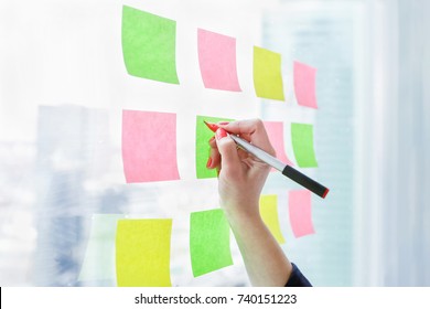 Creative woman writing on blank sticky notes on window in the office. Woman hand close-up - Shutterstock ID 740151223
