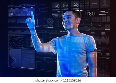 Creative work. Cheerful young programmer enjoying creating new useful programs and smiling while touching the icons on the transparent screen