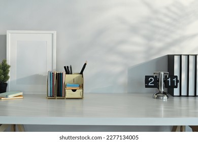 Creative workplace with blank picture frame, books and stationery on table with leaves shadow and sunlight - Shutterstock ID 2277134005