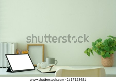 Creative workspace with blank tablet screen, framed photo and potted plant, ideal for showcasing productivity, or website mockups.