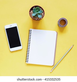 Creative Workspace Desk With Notebook, Smartphone, Pencil And Cactus On Yellow Background