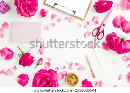 Creative workspace flat lay with pink roses, petals, notebook, scissors, and envelope on white background.