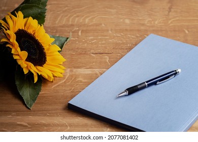 Creative writing time with a blue notebook, pen and fresh sunflower on the wooden table.