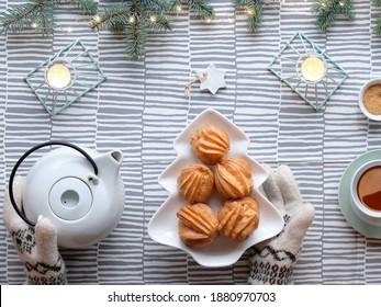 Creative Xmas table setup for tea with cakes. Creative flat lay with yummy eclairs or brewing cakes. Christmas tree shape plate with cakes. Fir twigs with light garland on stripy textile tablecloth.