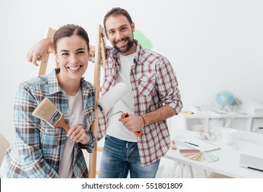 Creative young couple renovating their house and painting walls, they are posing together and smiling at camera