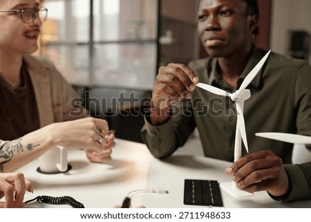 Creative young engineers sitting at table in office, working on new wind turbine design, medium closeup