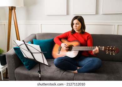 Creative Young Woman Singing And Playing The Guitar While Reading A Sheet Music And The Lyrics Of A New Song 