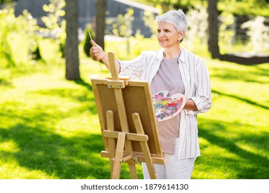 creativity, art and hobby concept - senior woman with easel and color palette painting outdoors - Powered by Shutterstock