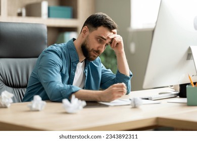 Creativity Crisis. Stressed young businessman sitting at desk in office and crumpling paper in despair, millennial male entrepreneur suffering lack of inspiration, having problems with project - Powered by Shutterstock