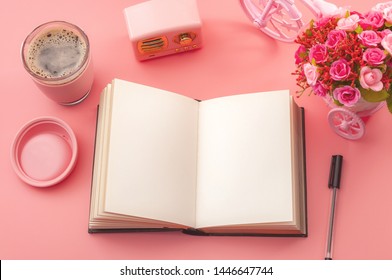 Creativity inspiring workplace concept with top view of a desk, vintage radio, hot cup of coffee and a pen next to a open book or journal isolated on pink background with copy space on the blank page