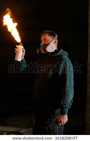 A creator in a dark studio holds a spray can that produces flames, wearing a mask for safety. The unique activity blends art and fire, showcasing creativity in a nighttime setting.