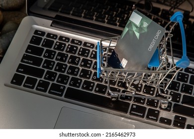 A credit card in a Mini supermarket trolley on a laptop keyboard. E-commerce and online shopping concept. Ideas about home shopping or buying things in virtual malls  stores from home or office.