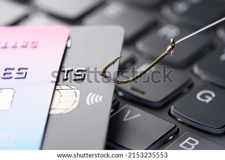 Credit card on fishing hook pulled from stack on keyboard, phishing scam data theft concept