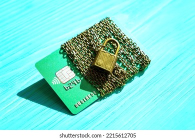 Credit Card Wrapped With A Bronze-toned Chain And Secured With A Massive Padlock Isolated On A Blue Wooden Background. E-commerce Fraud Protection Concept.