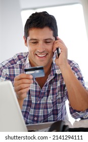 Credit Cards Come In Handy For Online Purchasing. Shot Of A Smiling Man On The Phone Holding Up A Credit Card While Sitting At His Desk.