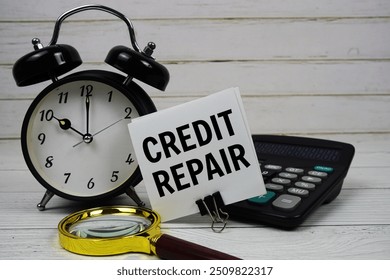Credit Repair text on paper card with alarm clock, calculator and magnifying glass on wooden background