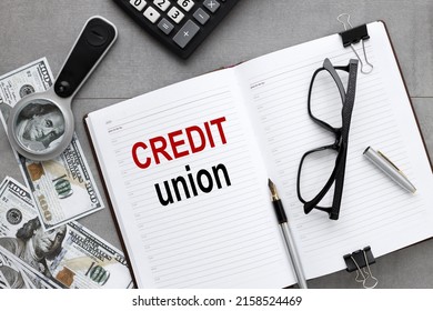 Credit Union. The Inscription On An Open Notepad, On A Gray Background A Dollar Bill Under A Magnifying Glass