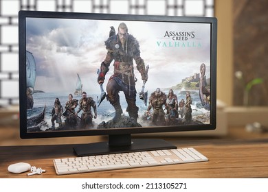 Assassin’s Creed Valhalla game on computer screen. Monitor, keyboard and airpods on wooden table. Selective focus. Rio de Janeiro, RJ, Brazil. October 2021.