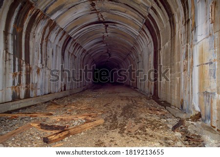 A creepy, abandoned,spooky railroad tunnel, with no light at the end of the tunnel.  There is a pile of debris, no tracks and several water stains running down the sides of the tunnel.