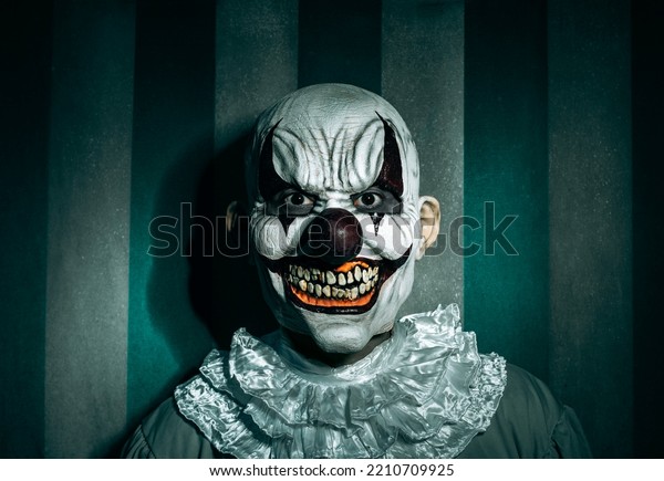 a creepy bald evil\
clown, in a gray costume with a white ruff around his neck, in\
front of a dirty and old circus tent, stares at the observer with a\
frightening smile 