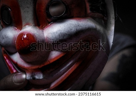 Creepy clown figure in the dark, hand holding an evil clown mask.