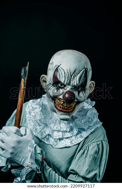 a creepy evil\
clown, wearing a gray costume with a white neck ruff, lifts an axe\
with stains of blood and menaces the observer with a frightening\
smile, on a black background