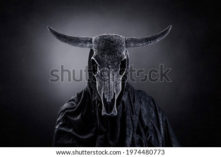 Creepy figure with animal skull with horns in the dark