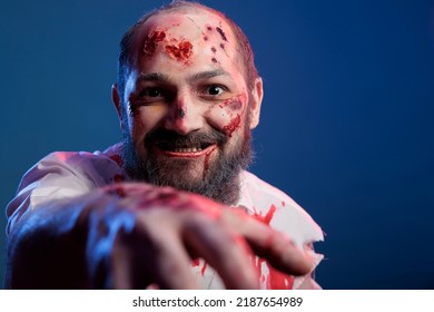 Creepy halloween zombie approaching camera in studio, looking spooky and dangerous with bloody scars and wounds. Apocalyptic sinister monster corpse with scary face and crazy eyes eating brain.