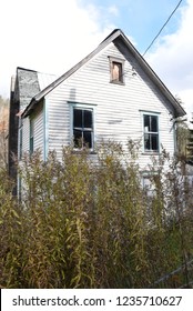 Creepy Haunted Neglected House From Back View With Weeds That Nearly Swallow Up The House.  Boarded Up, Weathered, Abandoned, Ugly, Historic, Empty.