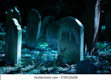 Creepy old cemetery in the night. Horror mysterious burial scenery. Blue moonlight on graves and grass. Scary dark background. Close-up image.