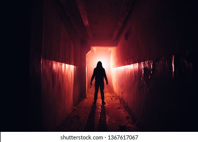 Creepy Silhouette With Knife In The Dark Red Illuminated Abandoned Building. Horror About Maniac Concept.