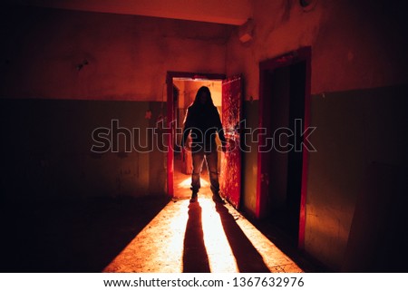 Creepy silhouette with knife in the dark red illuminated abandoned building. Horror about maniac concept.