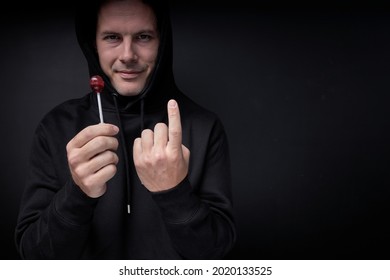 creepy threatening adult man in black wear offering candy lollipop to children standing on black studio portrait of caucasian maniac pedophile male looking at camera confidently, smiling terrible