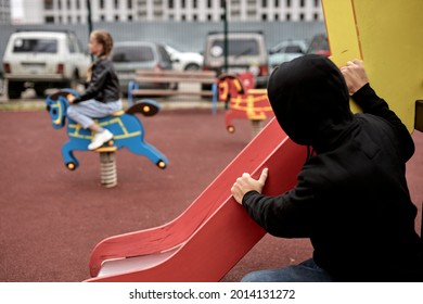 creepy threatening pedophile spies on child girl while having fun in playground alone, in casual wear at day time in city. dangerous man commit a crime, children abuse concept. focus on man