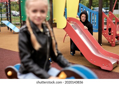 creepy threatening pedophile spies on child girl while having fun in playground alone, in casual wear at day time in city. dangerous man commit a crime, children abuse concept. focus on man