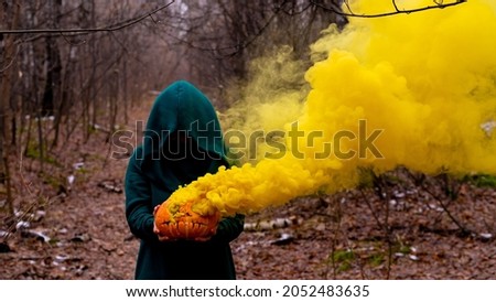 A creepy witch holds a steaming pumpkin in a deep forest. Jack o lantern emits yellow smoke for halloween