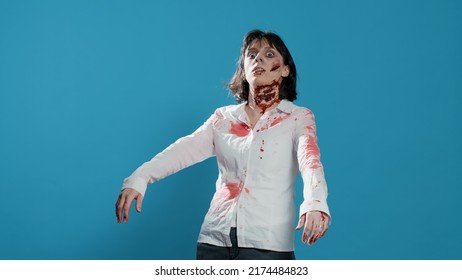Creepy zombie woman acting bizarre and sinister while growling on blue background. Mindless brain-eating evil monster with deep and bloody wounds and scars looking at camera. Studio shot