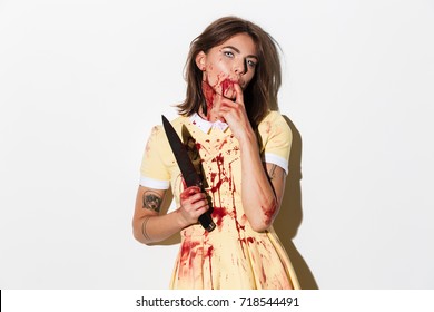 Creepy zombie woman covered in blood stains holding a knife and looking at camera isolated over white background
