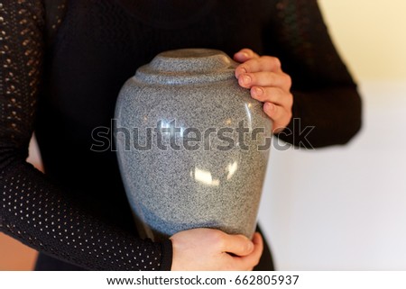 cremation, people and mourning concept - close up of woman with cinerary urn at funeral